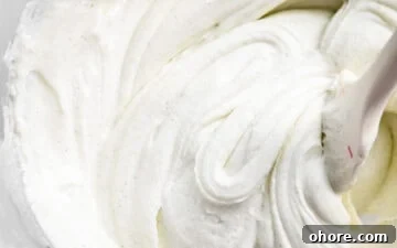 Cream Cheese Frosting with 5 Simple Ingredients 10 Close up of smooth cream cheese frosting and a silicone spatula inside a clear mixing bowl.