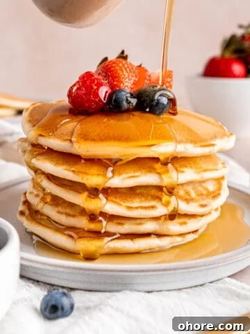 Pouring maple syrup over a stack of sourdough discard pancakes.
