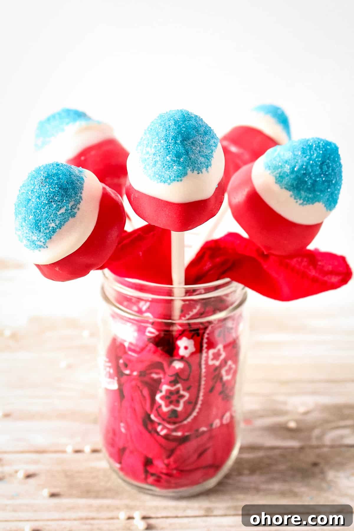 Sparkling Strawberry Firecracker Pops: Patriotic Summer Treats 2 Red, white, and blue covered strawberries on sticks in a mason jar. The mason jar has a red bandana stuffed in it.