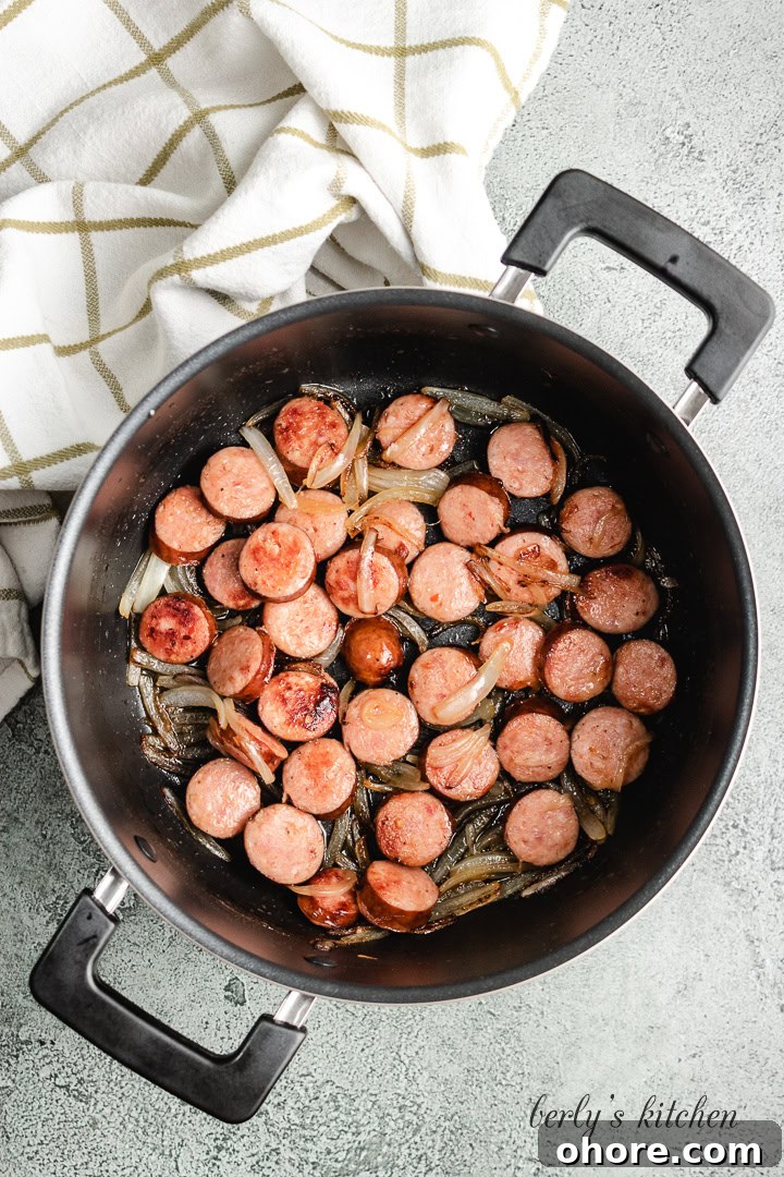 Creamy Kielbasa Pasta Recipe with Garlic Parmesan Sauce 3 Sausage and onions cooking in a pot.