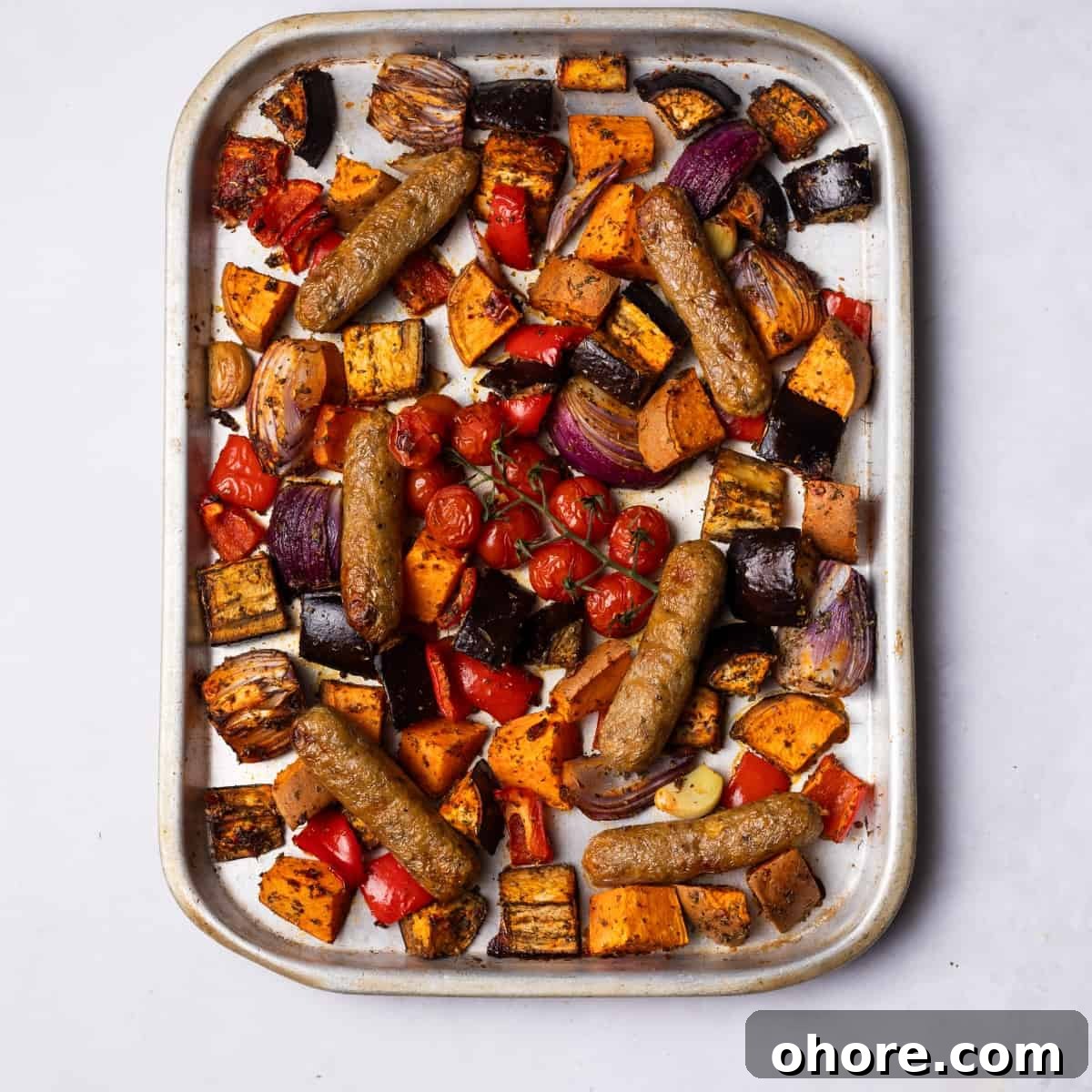 Sausages baked on the tray with colourful vegetables.