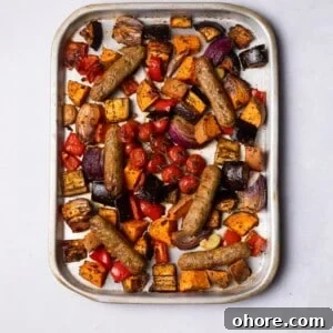 Sausages baked on the tray with colourful vegetables.