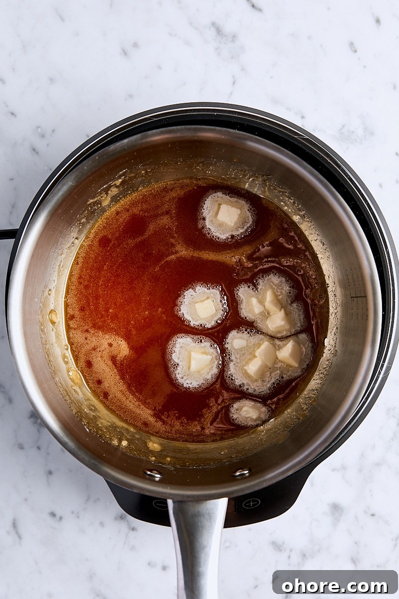Cubed butter added to caramel mixture in light-colored saucepan