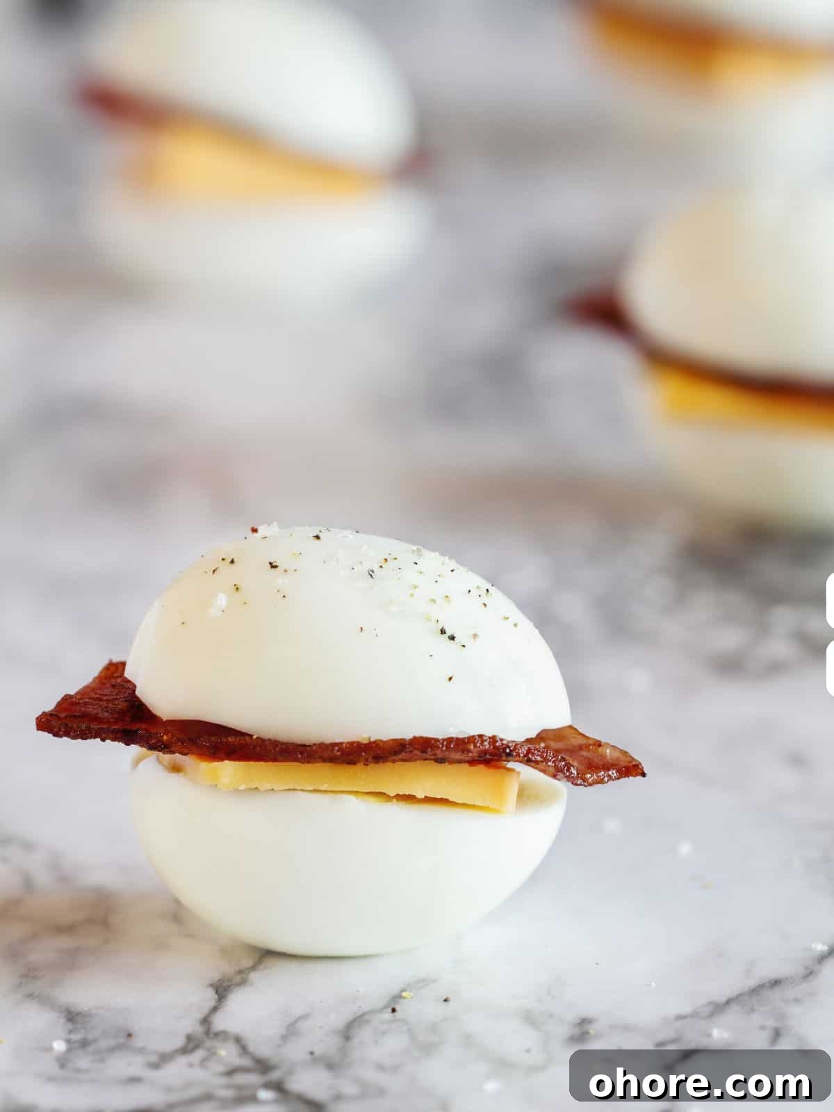 Keto-Friendly Travel Snacks for Low-Carb Trips 2 Close-up of a hard-boiled egg slider with bacon and cheese on a marble surface, perfect as keto travel snacks. Similar sliders are blurred in the background, offering a delectable glimpse into your next on-the-go meal.