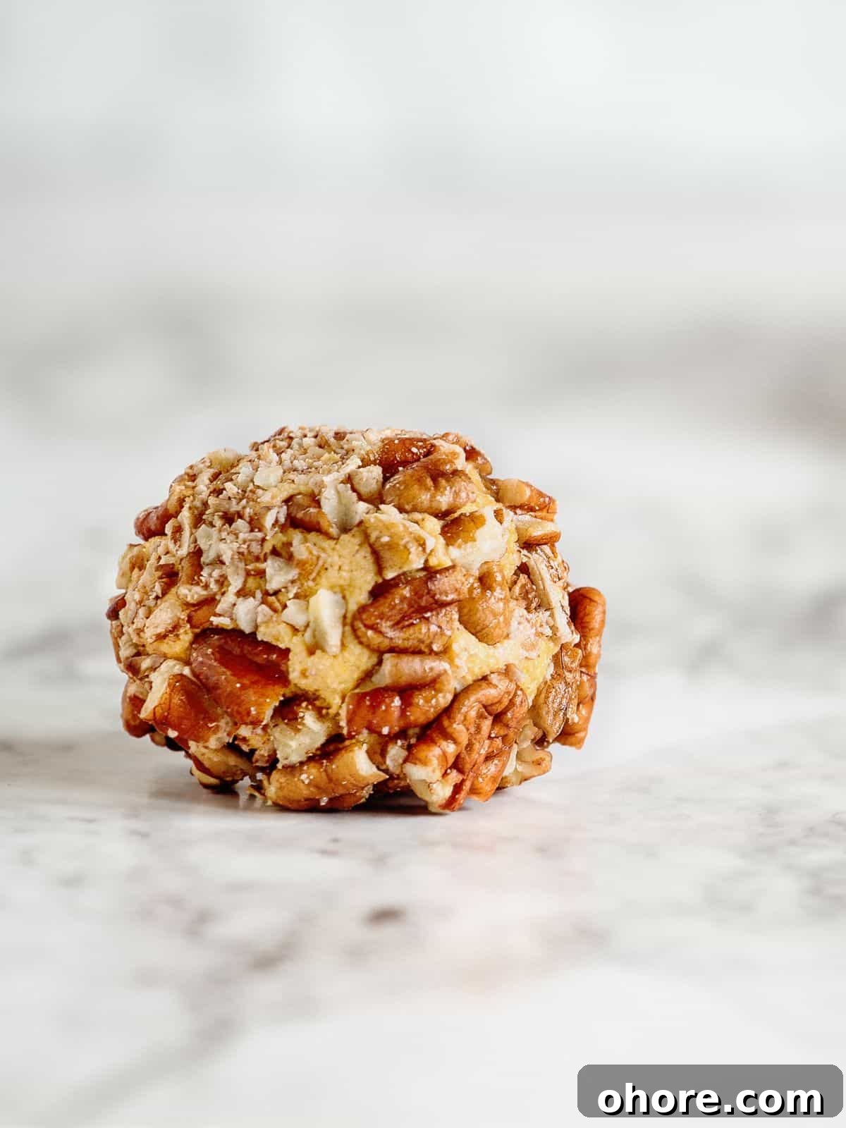 Keto-Friendly Travel Snacks for Low-Carb Trips 4 A cheese ball, perfect for keto travel snacks, is coated with chopped nuts and rests elegantly on a marble surface.