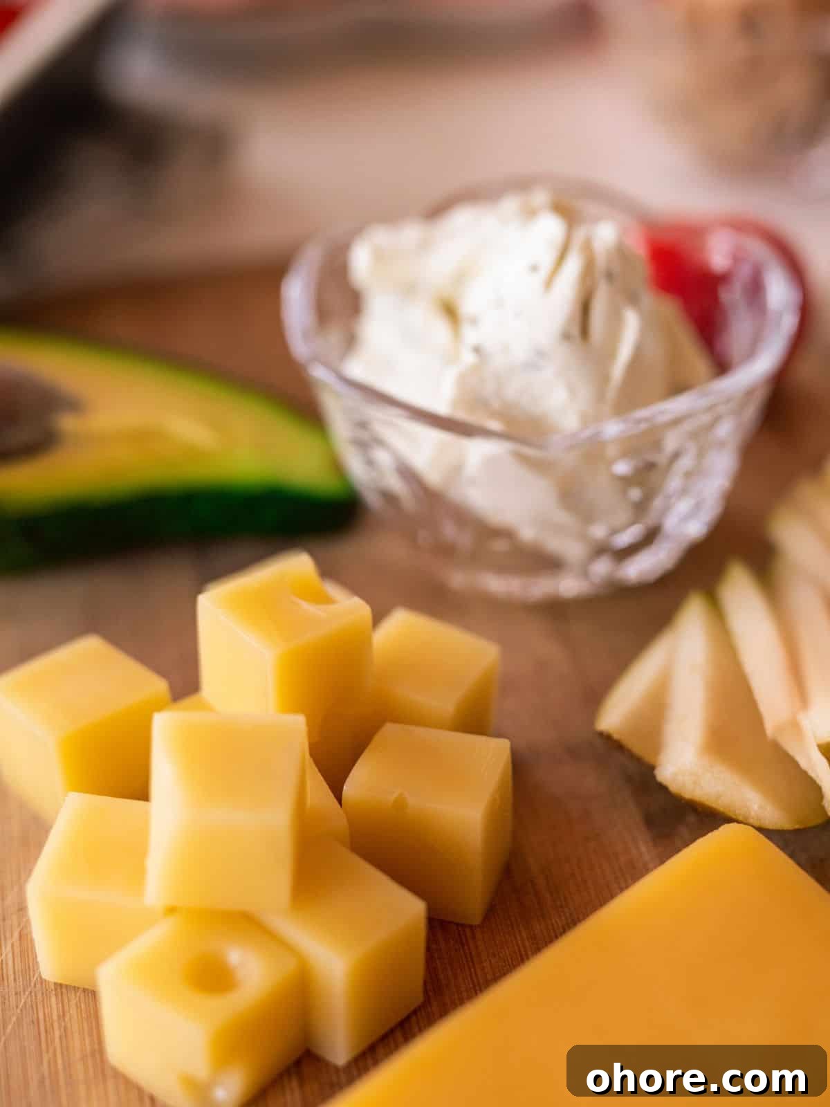 Keto-Friendly Travel Snacks for Low-Carb Trips 6 Close-up of cubed cheese, sliced avocado, and a small bowl of creamy cheese on a wooden board—perfect keto travel snacks for your next adventure.