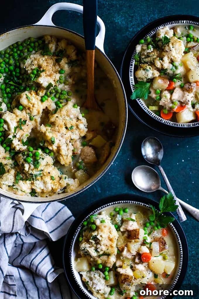Easy Chicken and Dumpling Soup An overhead shot of a dutch oven of Easy Chicken and Dumpling Soup, two bowls of soup, two spoons and a striped napkin on a green speckled surface.
