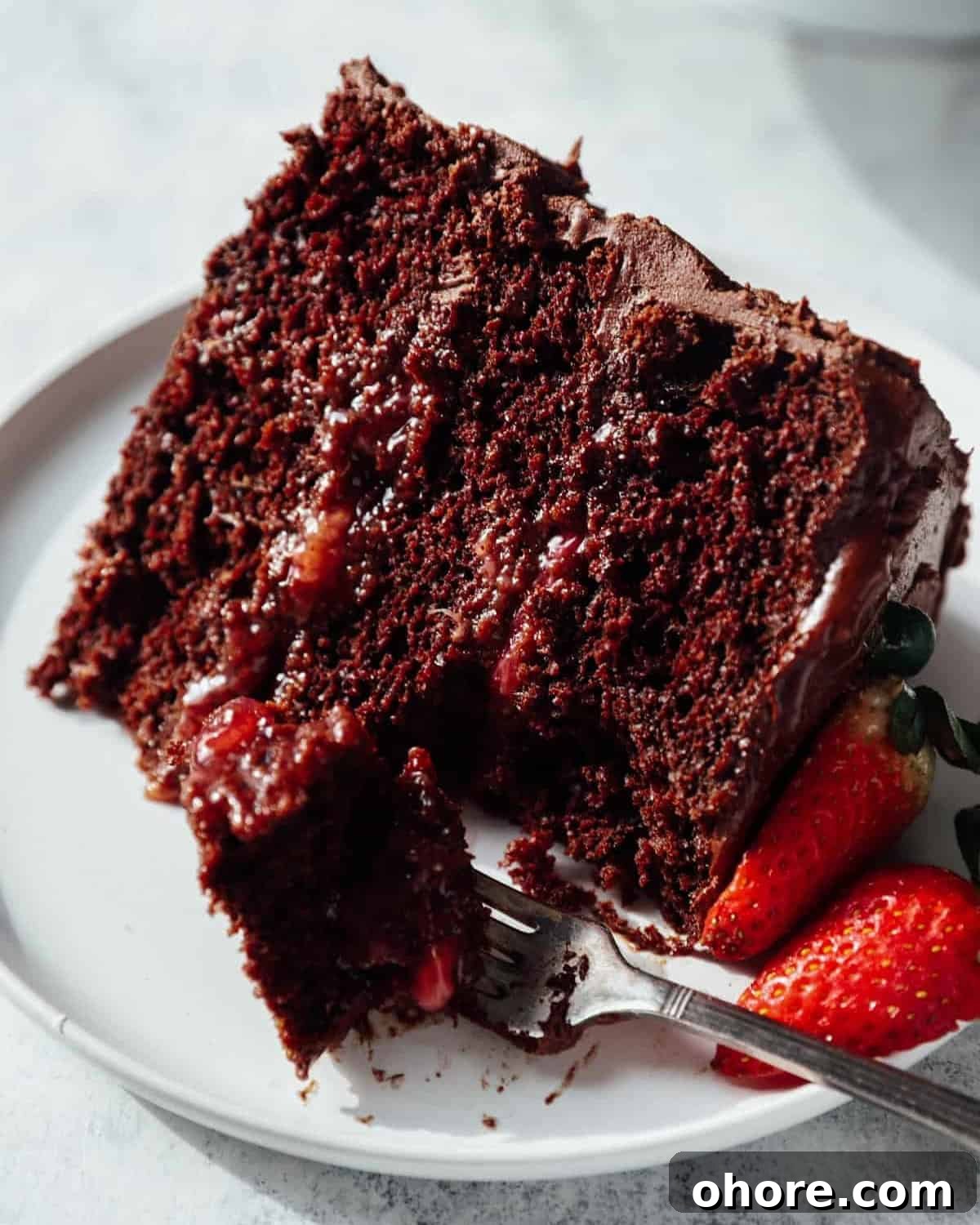 Decadent Chocolate Strawberry Layer Cake Recipe 3 a partially eaten slice of chocolate strawberry cake on a plate with a fork.