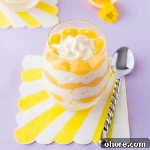 A lemon cheesecake cup - layered cheesecake in a stemless wine glass, on a light purple background.