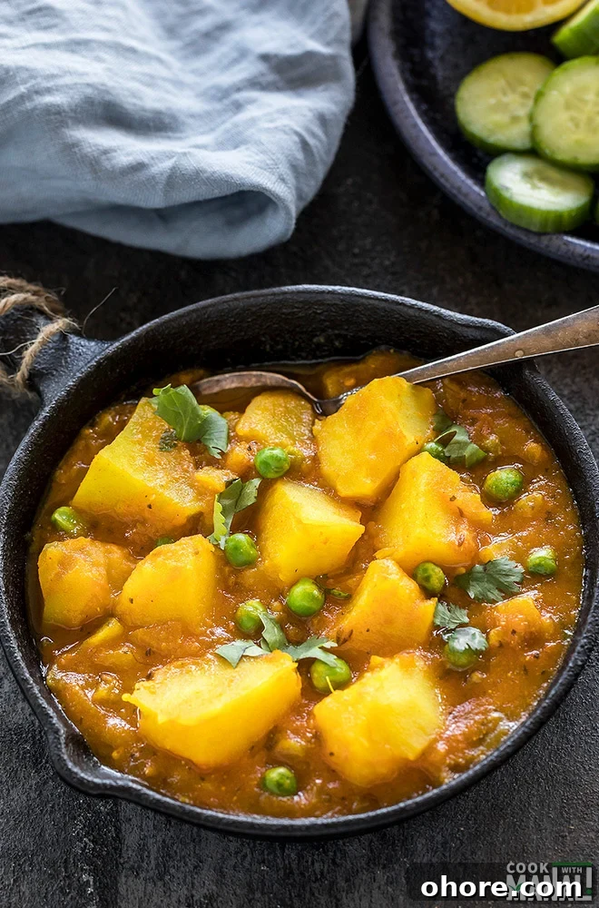 Instant Pot Aloo Matar (Potatoes and Peas Curry) 3 instant pot aloo matar served in a small black skillet with a spoon on the side