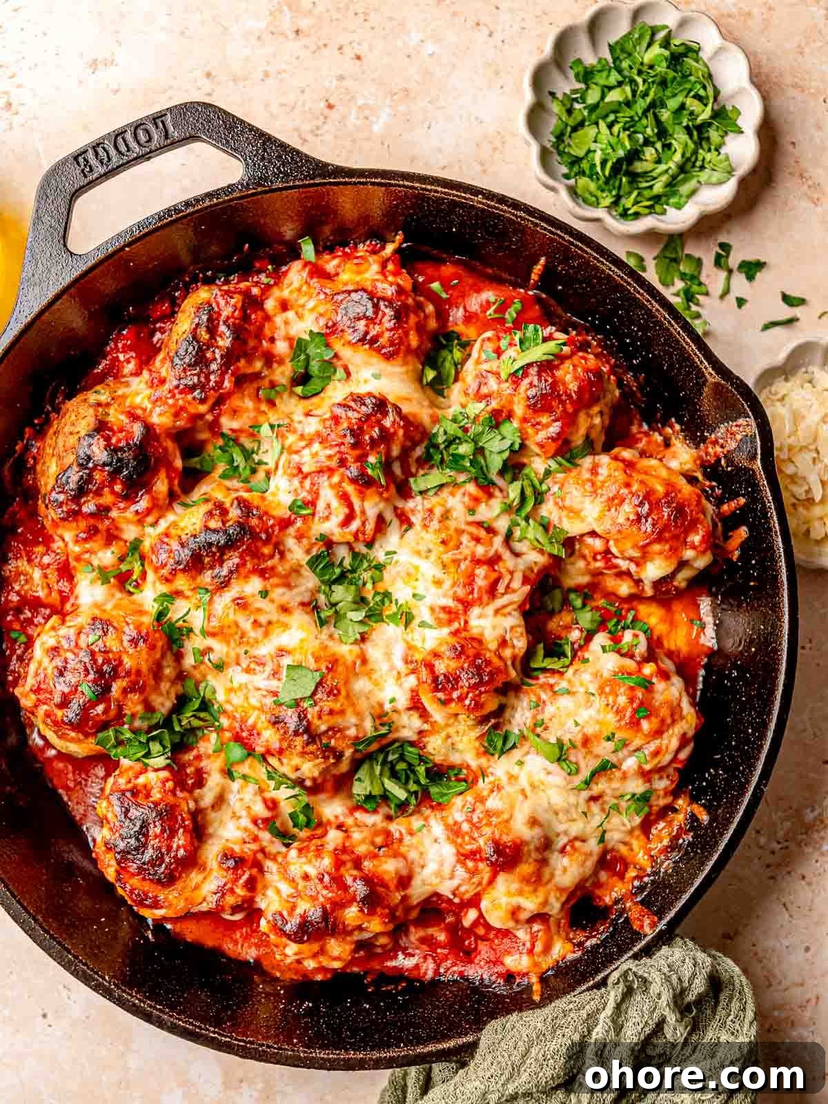 Baked Chicken Parmesan Meatballs Recipe That Melts in Your Mouth 2 A cast iron skillet filled with baked meatballs topped with cheese and chopped parsley.