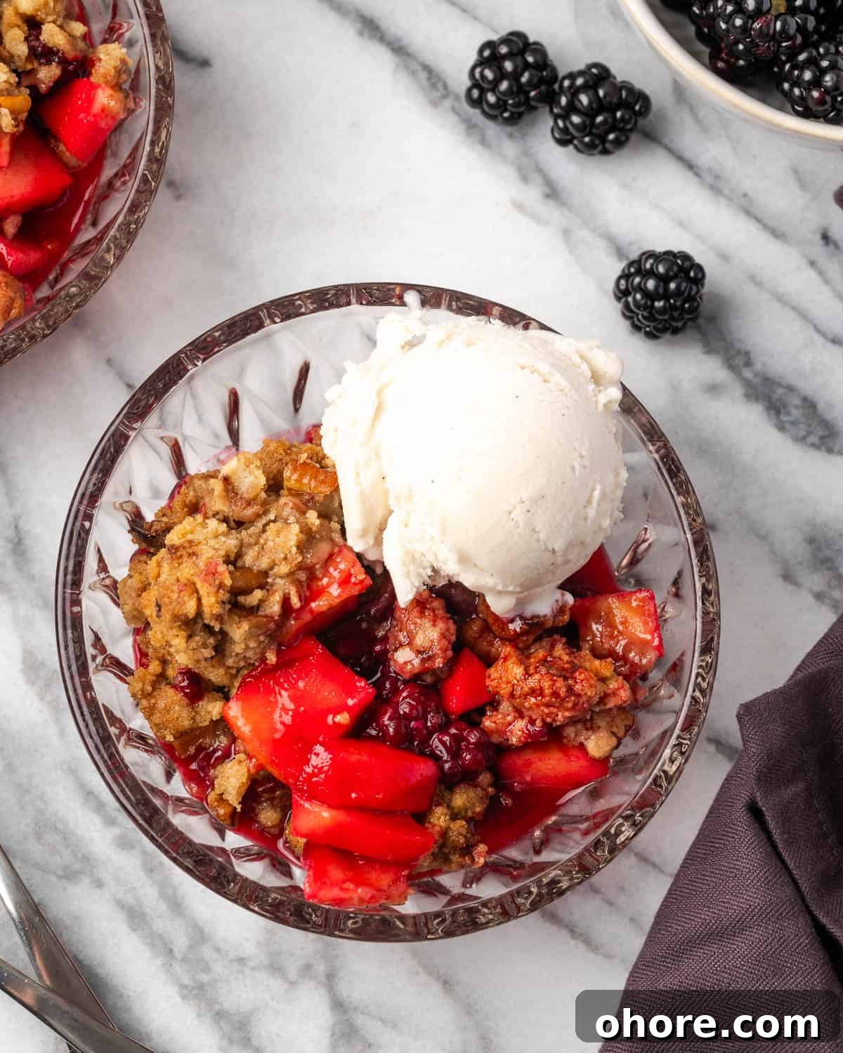 Apple & Blackberry Crumble Recipe: Rustic Autumn Dessert 2 A bowl of apple blackberry crumble topped with vanilla ice cream sitting on a marble counter.