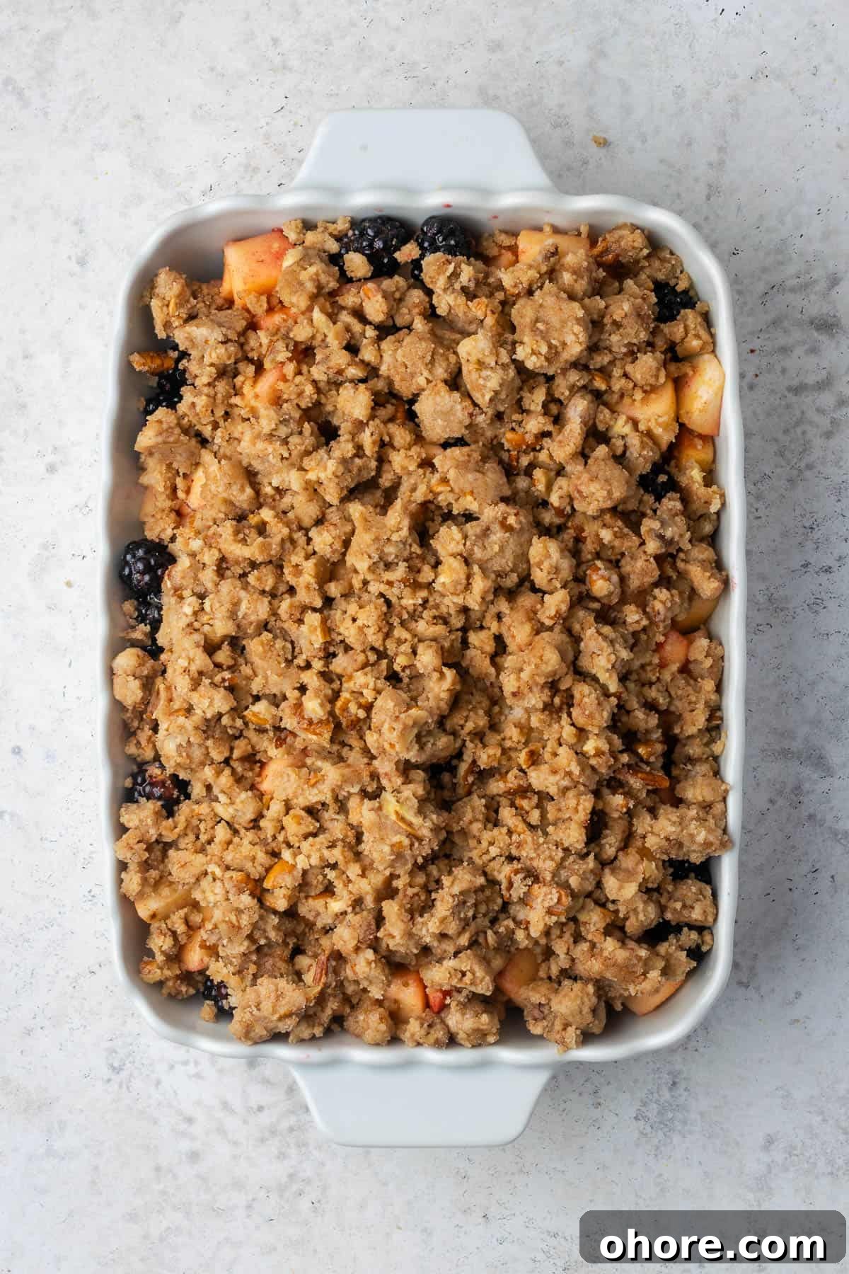 Apple & Blackberry Crumble Recipe: Rustic Autumn Dessert 7 An unbaked apple and blackberry crumble sitting on a white counter.