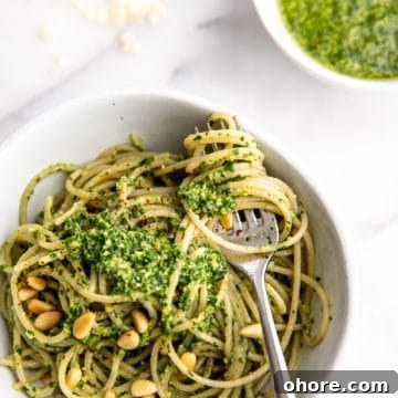 Spaghetti in bowl topped with green sauce, with fork