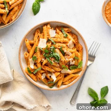 Tomato pesto pasta in a bowl, topped with basil and shaved parmesan cheese.