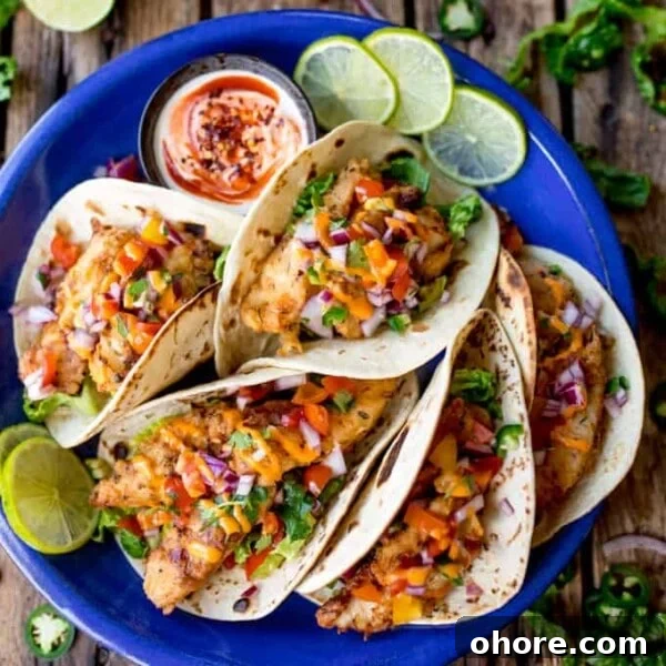 Overhead square image of 6 crispy fish tacos on a blue plate, topped with pico de gallo and sriracha mayo.