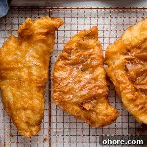 Three golden battered fish fillets on a copper wire rack topped with sea salt flakes.