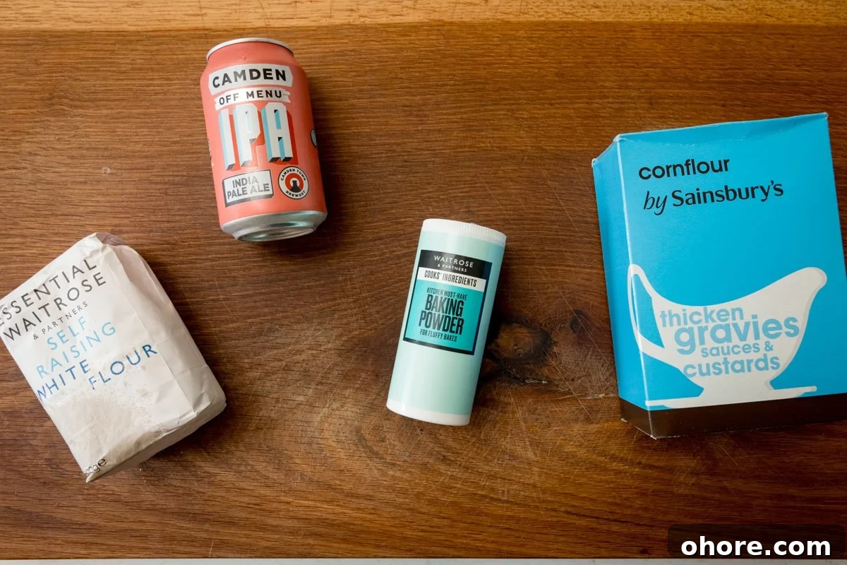An overhead shot of the ingredients for the beer batter is laid out on a wooden board. They are as follows: self-raising white flour, IPA (beer), baking powder, and cornflour.