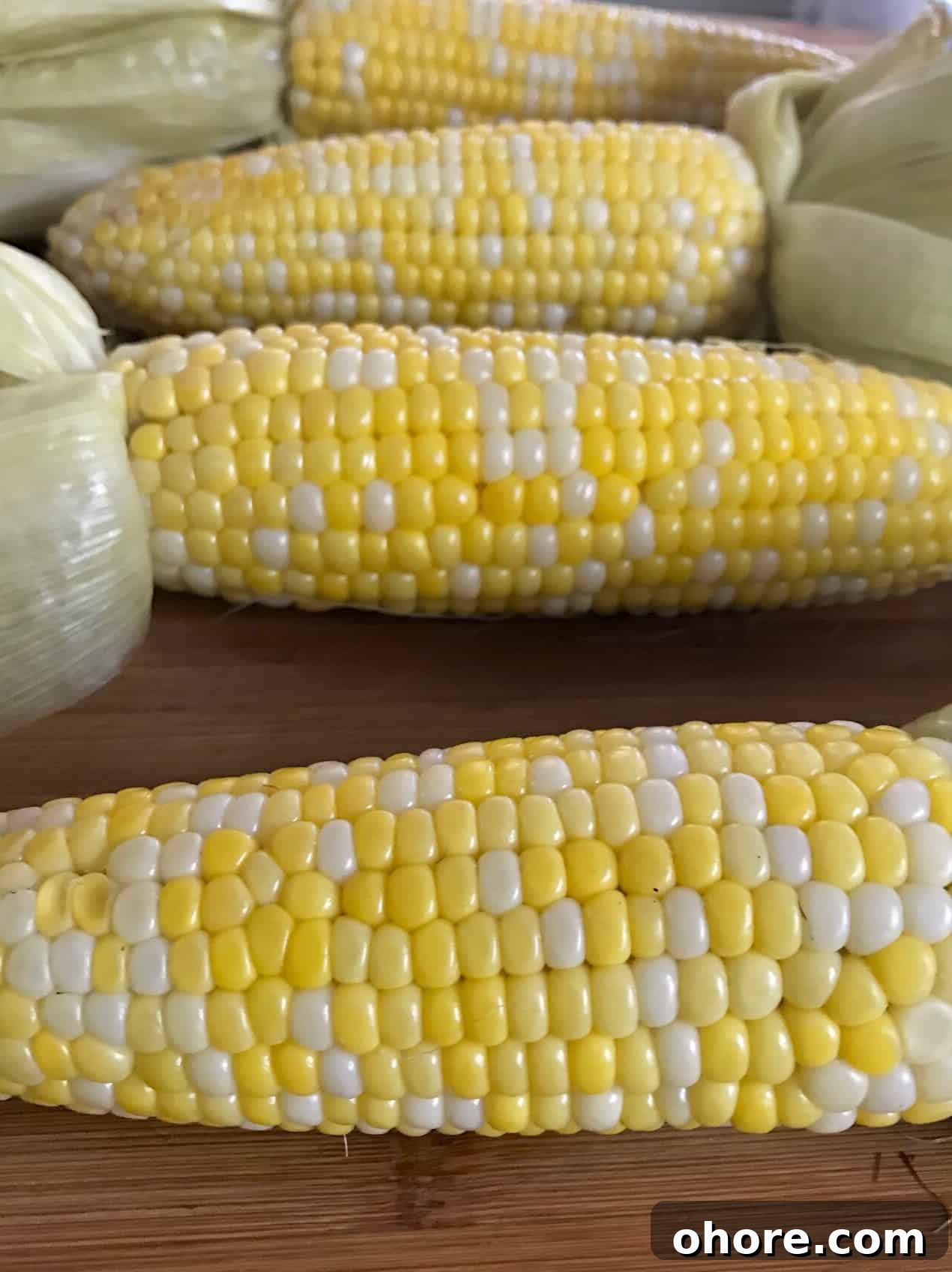 Corn on the cob with husks pulled back on wooden board close up side view