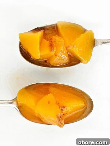 Two silver spoons with peach compote on a white surface.