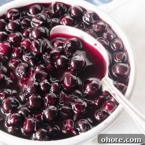Blueberry Compote Recipe: Simple Homemade Blueberry Sauce 12 Very close up image of blueberry compote in white bowl with silver spoon.