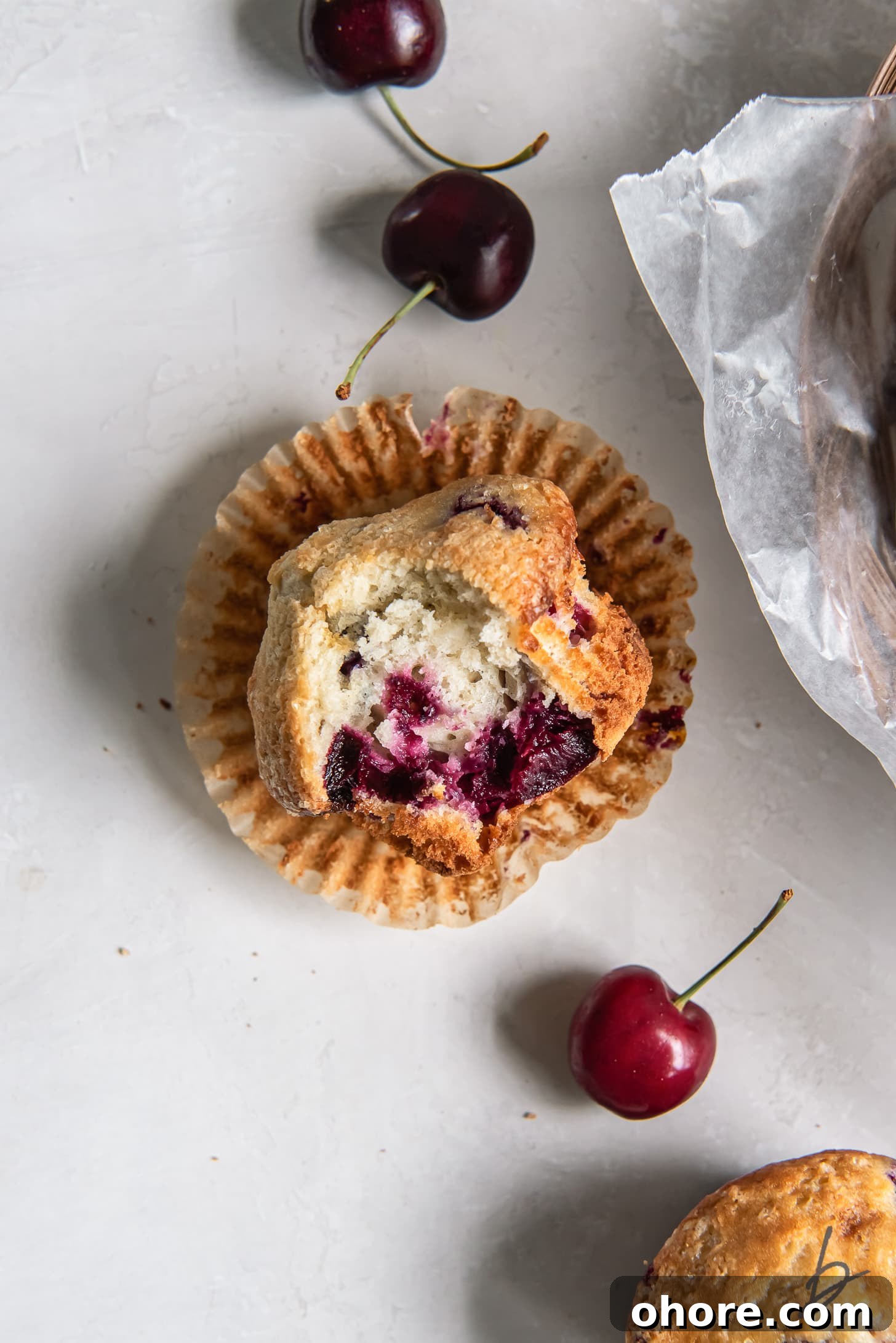 Cherry Almond Muffins: Homemade Cherry Muffin Recipe with Almond Extract 7 cherry muffin with a bite laying on its side on open paper muffin liner