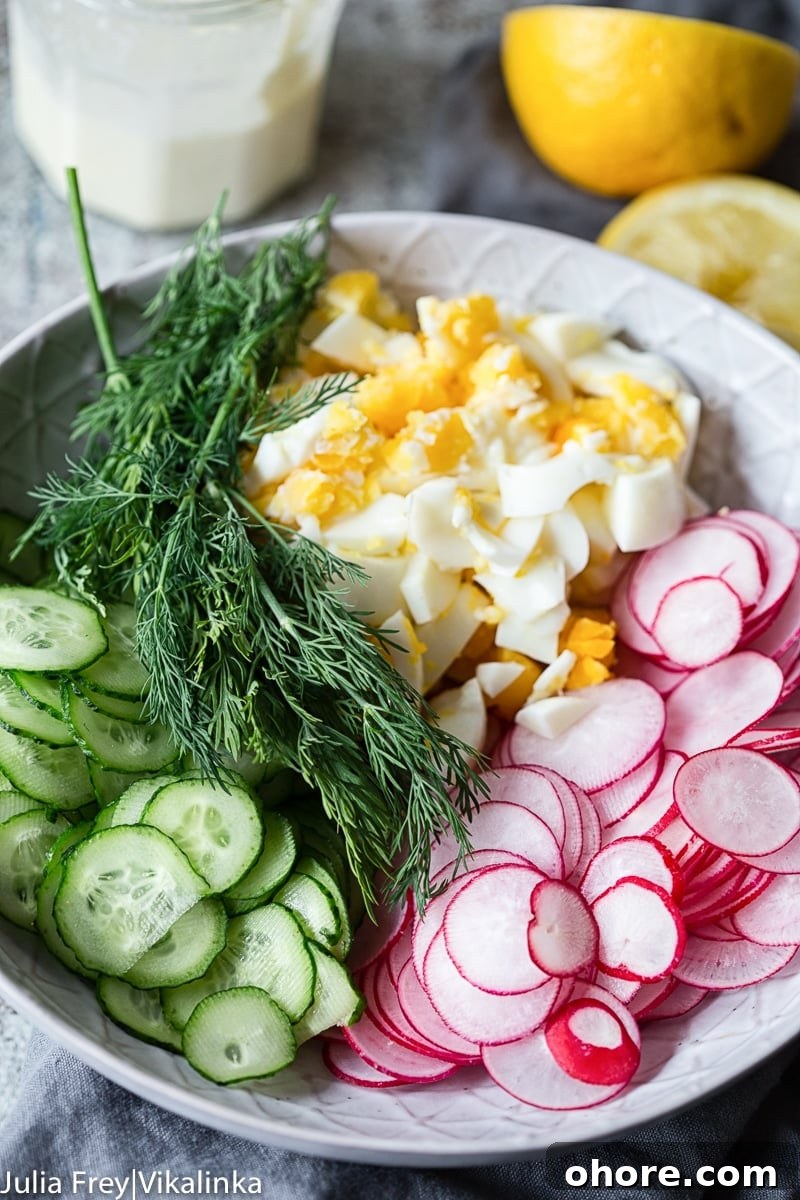 Creamy Dill Cucumber, Radish & Egg Salad Recipe 3 sliced cucumbers, radishes, chopped hard boiled eggs and fresh dill in a bowl, lemon in the background.