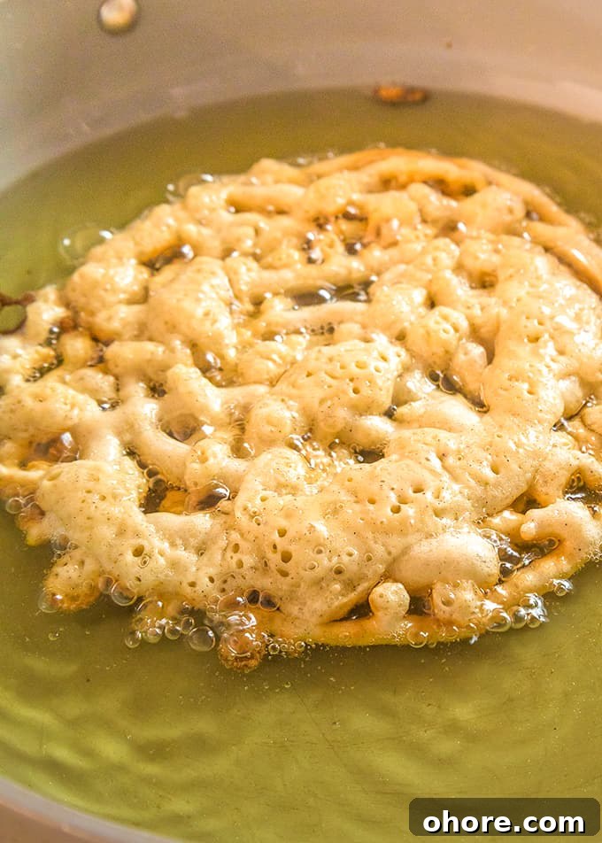 Crispy Homemade Funnel Cake Recipe for Fair-Style Treats 5 A homemade funnel cake is being cooked in a frying pan with canola oil