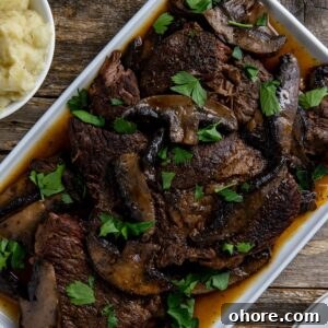 Keto Dutch Oven Pot Roast Recipe — Tender Low-Carb Roast 15 Cooked sliced roast topped with mushrooms and sliced portobella mushrooms on a white serving platter.