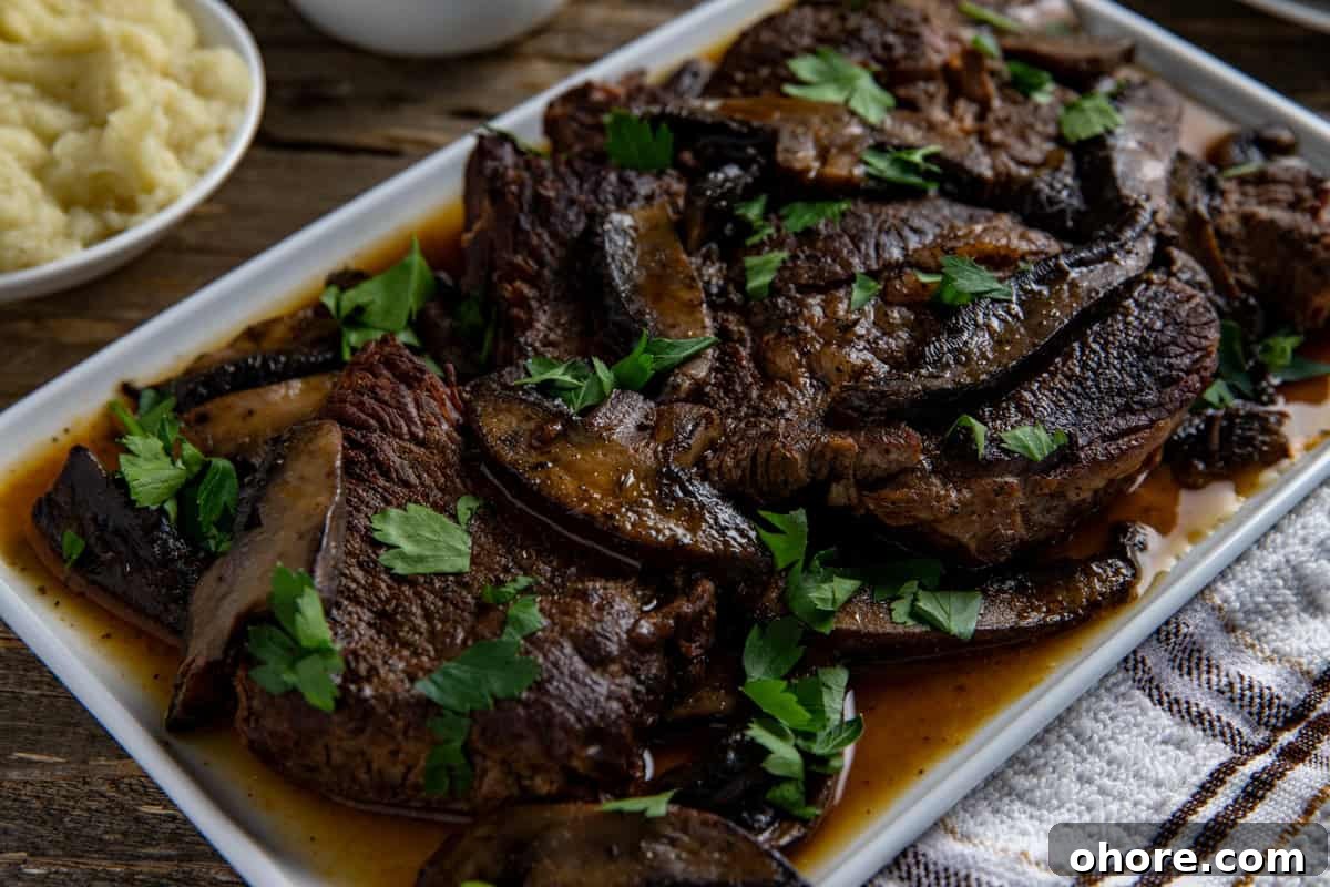 Keto Dutch Oven Pot Roast Recipe — Tender Low-Carb Roast 9 Cooked sliced roast topped with mushrooms and sliced portobella mushrooms on a white serving platter.