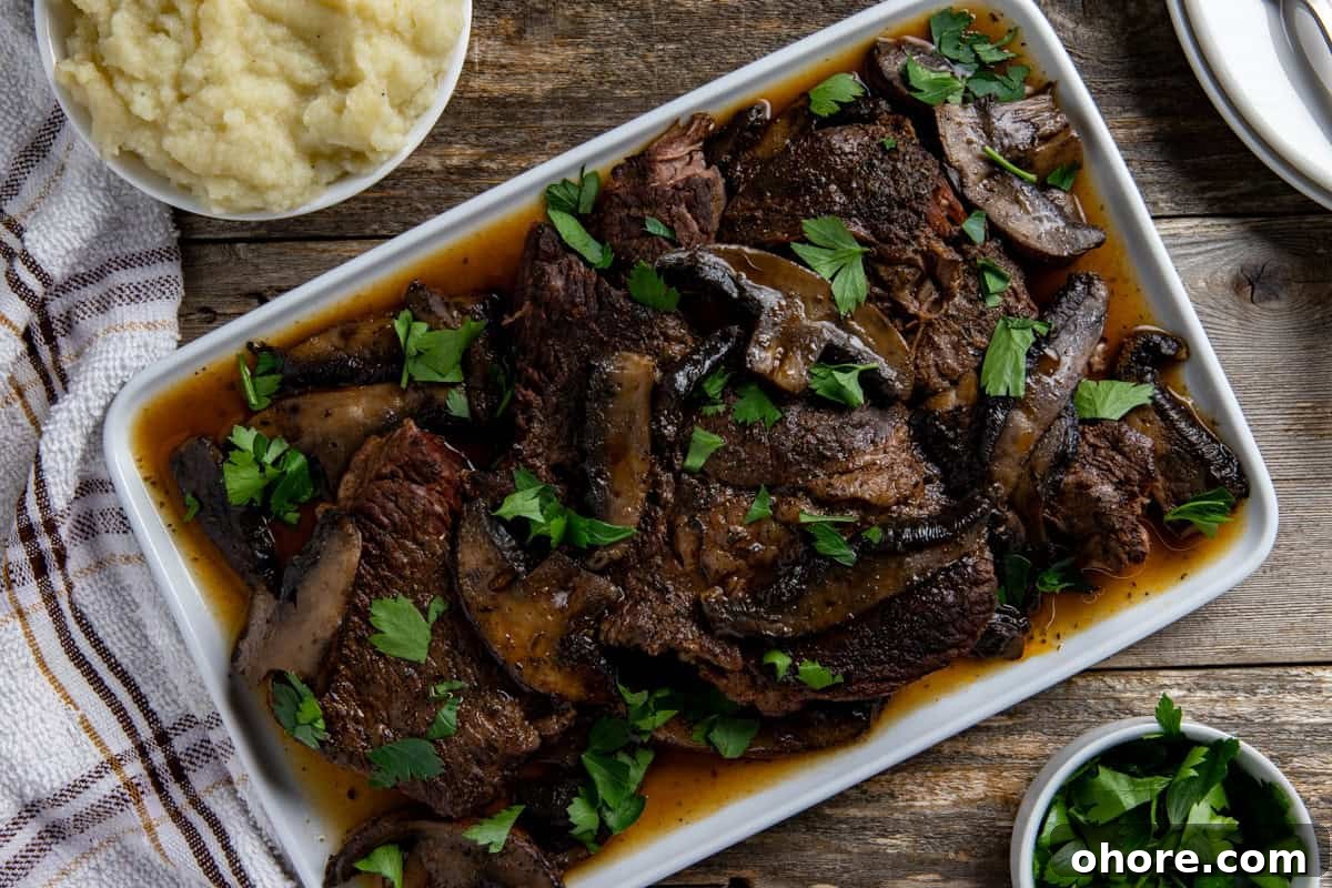 Keto Dutch Oven Pot Roast Recipe — Tender Low-Carb Roast 10 Cooked sliced roast topped with mushrooms and sliced portobella mushrooms on a white serving platter.