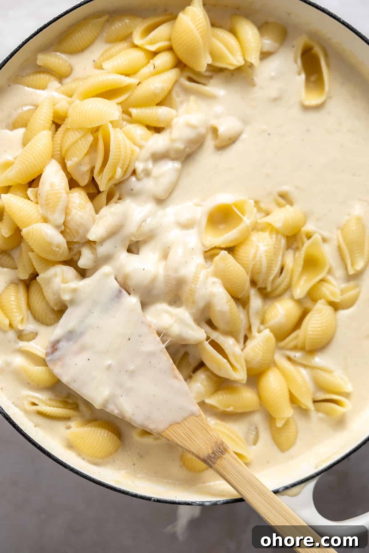 Creamy White Cheddar Macaroni and Cheese Recipe 7 stirring cooked pasta shells into a white cheddar sauce on the stove top.
