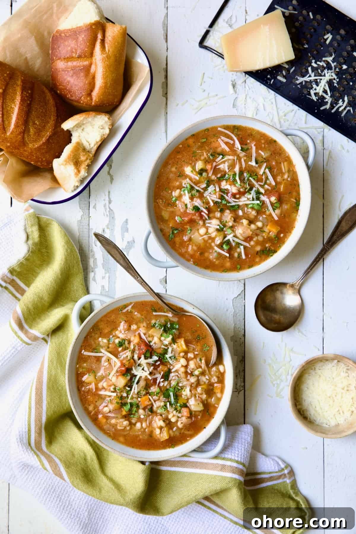 Hearty Vegetable and Barley Soup Recipe for Comforting Meals 10 Two bowls of Vegetable Barley Soup on white distressed background with bread and cheese.