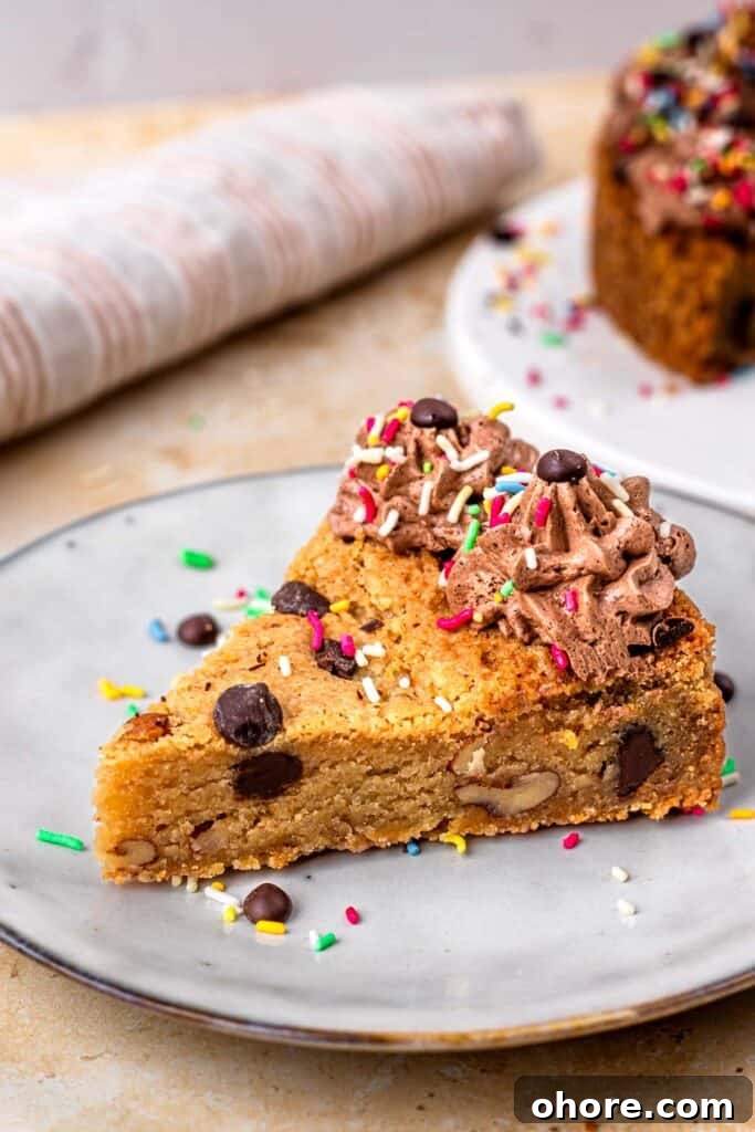 Gluten-Free Cookie Cake Recipe: Soft, Chewy Sugar Cookie Cake 3 Slice of a gluten free cookie cake topped with chocolate buttercream on the outside, sprinkles and chocolate chips, sitting on a white plate, and surrounded by more sprinkles.