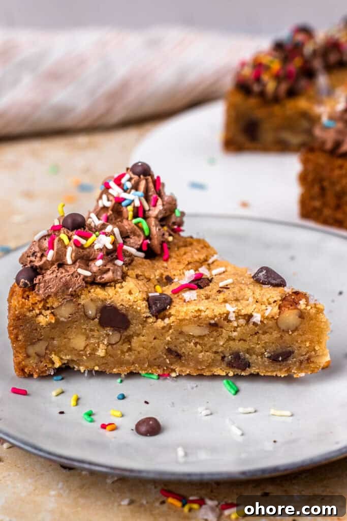 Gluten-Free Cookie Cake Recipe: Soft, Chewy Sugar Cookie Cake 9 Slice of a gluten free cookie cake topped with chocolate buttercream on the outside, sprinkles and chocolate chips, sitting on a white plate, and surrounded by more sprinkles.