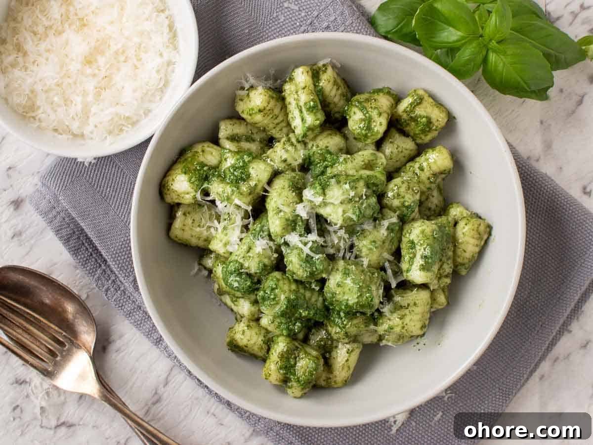 Creamy Pesto Gnocchi with Parmesan and Basil 5 A bowl of gnocchi on a grey cloth with bowl of grated parmesan on the side viewed from above.