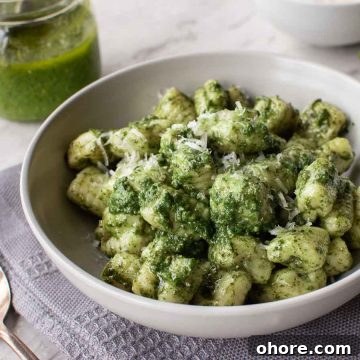 Creamy Pesto Gnocchi with Parmesan and Basil 6 a bowl of pesto gnocchi on a grey cloth with jar of pesto in the background.