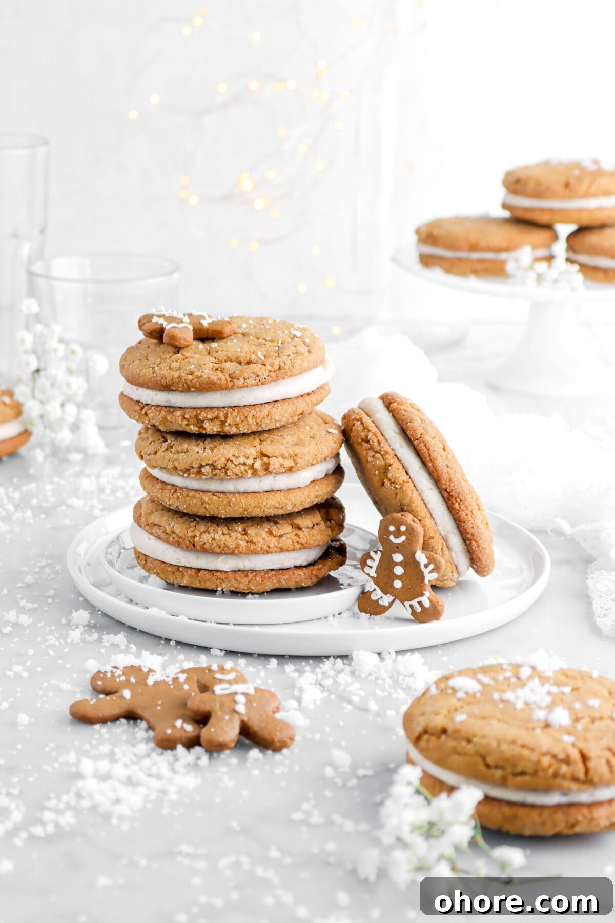 Gingerbread Sandwich Cookies Recipe for Holiday Parties 3 four gingerbread sandwich cookies on white plate with four mini gingerbread men cookies and three more cookies behind on white cake plate.