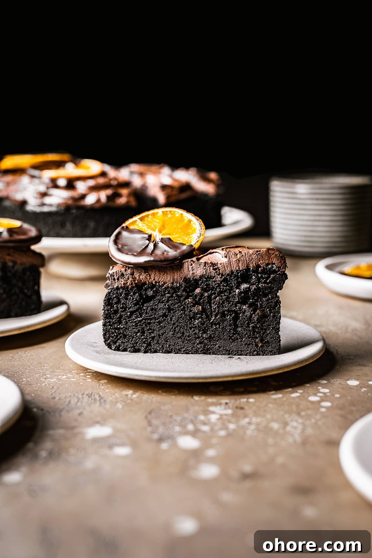 Decadent Chocolate Orange Cake Recipe for Irresistible Flavor 3 A slice of cake with thick chocolate frosting on a plate. A chocolate dipped dried orange slice sits on top.