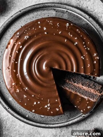 A chocolate ganache covered chocolate cake with a slice cut out and turned on an angle to show the inside.