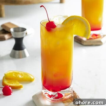 Vodka sunrise cocktail on table with cherry and orange slice.