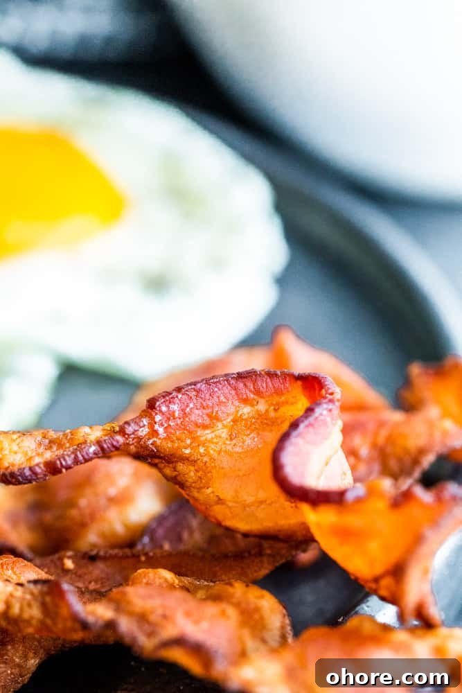 Close up of crispy bacon with egg in the background.