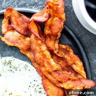 Bacon on a black plate with an egg and coffee on the side.