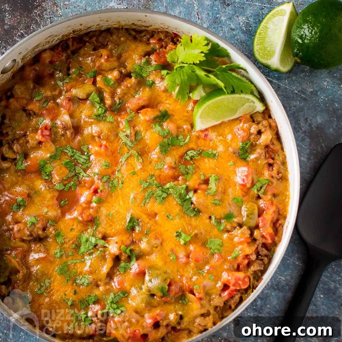 Quick Weeknight Dinners When You're Short on Time and Supplies 3 Overhead shot of cheesy taco meat garnished with fresh parsley and lime wedges in a black and white skillet on a whicker placemat.