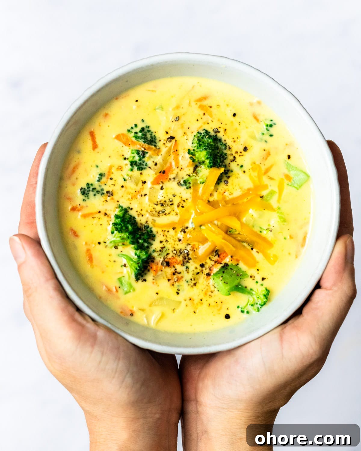 Creamy Broccoli Cheddar Soup Recipe for Cozy Comfort Meal 2 hands holding up a bowl of broccoli cheddar soup.