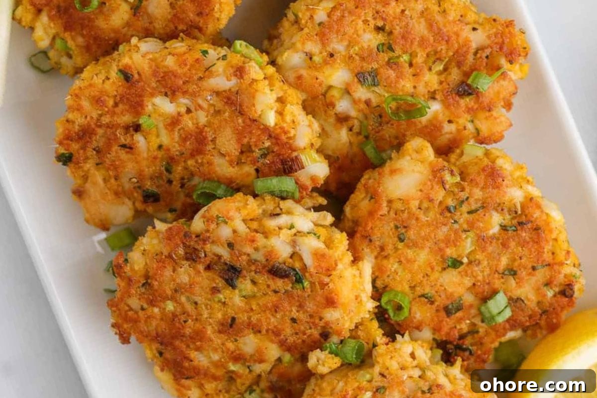 12 Spectacular Seafood Dinners for Meat-Free Weeknight Meals 11 Golden-brown seafood patties garnished with green onions, served on a white plate with a slice of lemon.