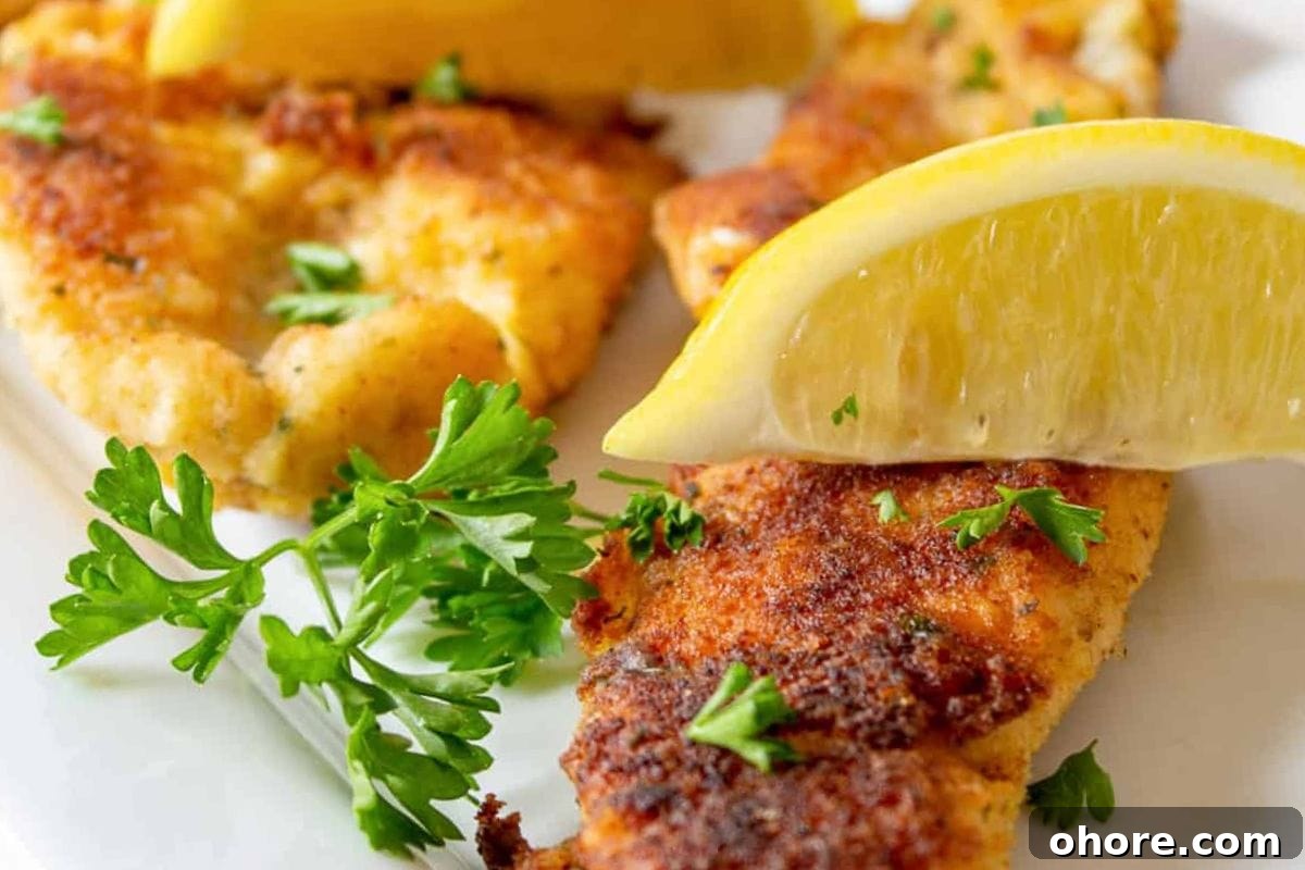 12 Spectacular Seafood Dinners for Meat-Free Weeknight Meals 4 A close-up of crispy pan-fried fish fillets garnished with fresh parsley and served with lemon wedges on a white plate.