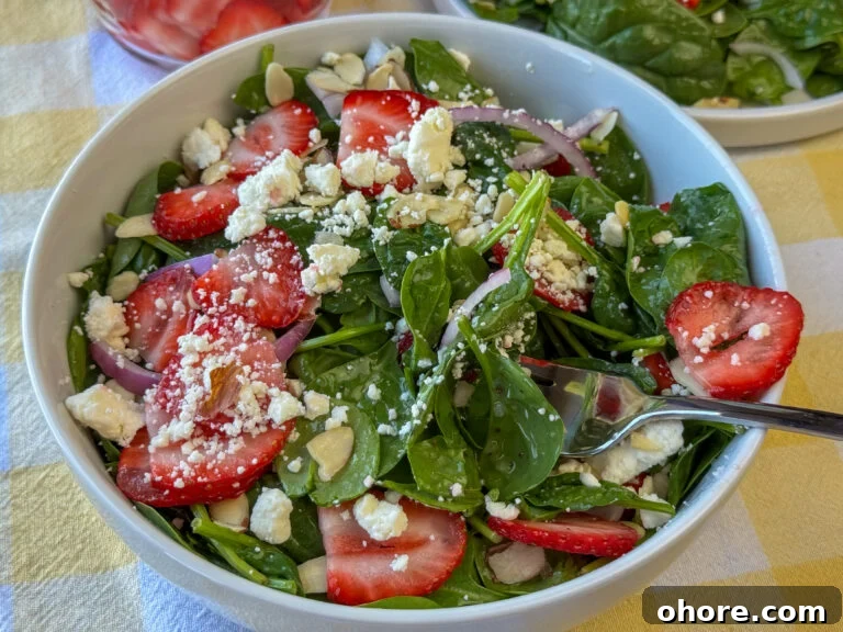 Bowl full of spinach salad with strawberries, feta and a light poppy seed dressing with a fork resting on the edge.