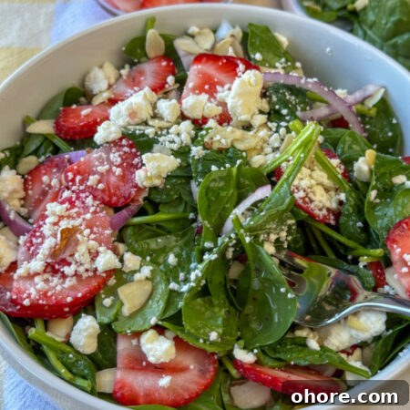 Fork in a delicious bite of an easy spinach salad with sliced strawberries, crumbled feta and a simple poppyseed dressing.