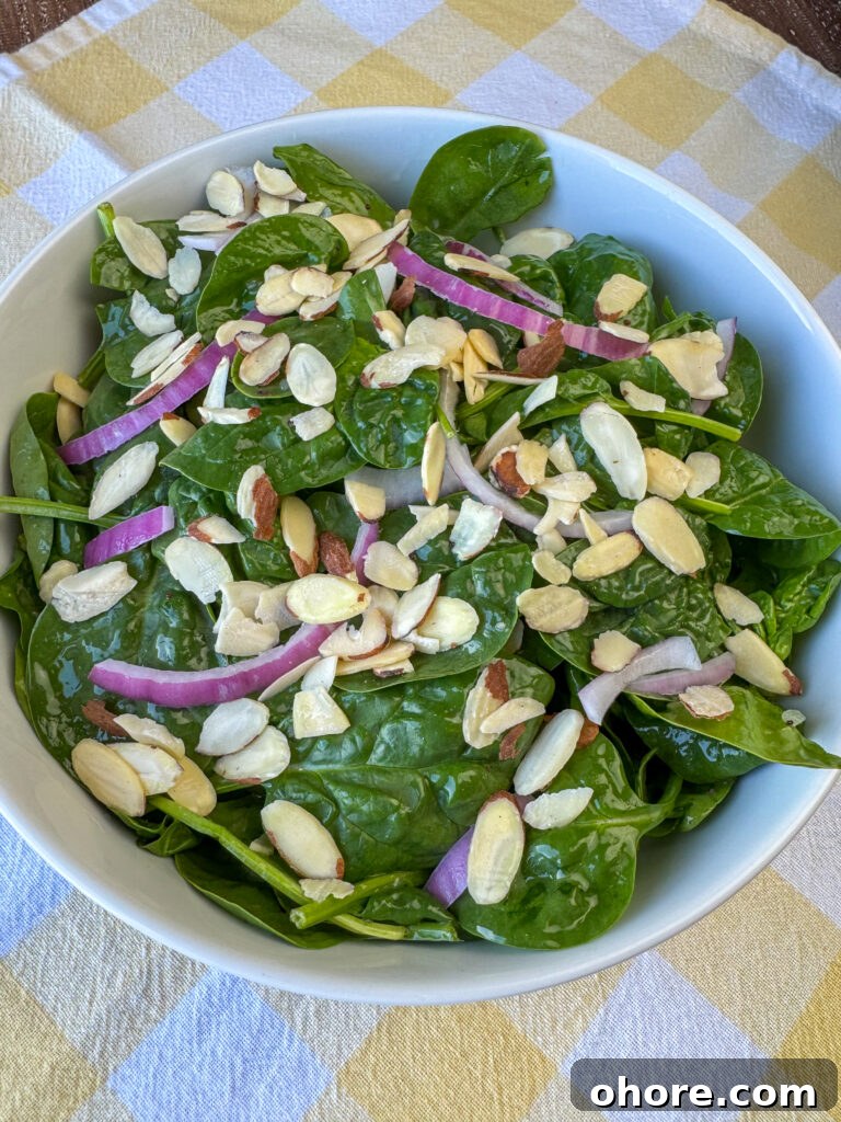 Almonds and red onion slices accenting baby spinach in a white bowl on a yellow and white plaid napkin.